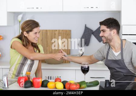 Komisches Paar, das beim Kochen so tut, als würde es sich mit Utensilien streiten Stockfoto