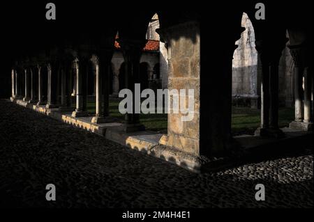 Das schräge Sonnenlicht im Dezember schafft tiefe Schatten in den Kopfsteinpflastergalerien des mittelalterlichen Klosters, das an die cathédrale Notre-Dame de Saint-Bertrand-de-Comminges, Haute-Garonne, Occitanie, Frankreich, angeschlossen ist, einer ehemaligen römisch-katholischen Kathedrale, die heute eine Pfarrkirche ist, die auch cathédrale Sainte-Marie genannt wird. Stockfoto