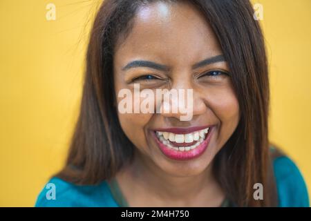 Porträt einer schönen braunen jungen, dunkelhäutigen Frau, die fröhlich lächelt - gelber Hintergrund Stockfoto