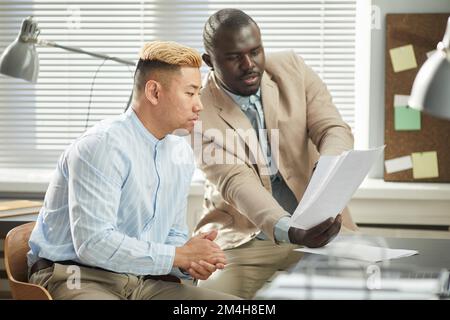 Seitenansicht von zwei ethnischen Führungskräften, die Dokumente lesen, während sie ein Projekt im Büro planen Stockfoto