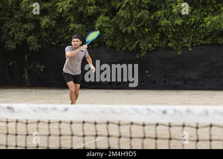 Ein junger bärtiger Mann mit Mütze spielt draußen Tennis. Männlicher Tennisspieler in Bewegung. Stockfoto