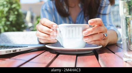 Frauenhände und weiße Kaffeetasse Nahaufnahme, Frau hält Tasse in der Hand, während sie im Straßencafé sitzt. Stockfoto