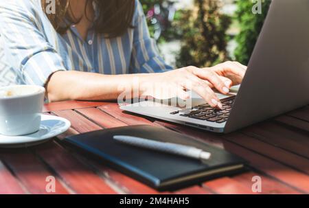 Weibliche Person, die ihren Laptop benutzt, während sie im Sommer im Café draußen sitzt. Stockfoto