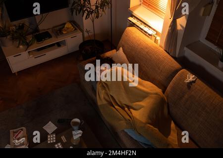 Grippe und psychologisches Problem. Draufsicht auf die Krankheit die junge Weiße liegt auf dem Sofa, das mit einer Decke bedeckt ist. Tisch mit Medizin und Pillen. Einsamkeit und Stockfoto