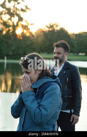 Der Junge sieht angewidert aus, wenn ein Mädchen sich eine Erkältung in die Nase bläst. Ekel zwischen zwei Freunden wegen Grippe. Outdoor-Szene in einem Park. Stockfoto
