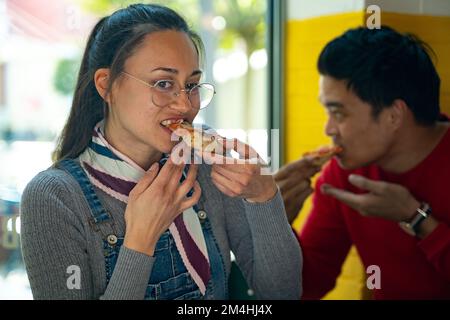 Ein vielseitiger Teammitarbeiter, der Pizza zusammen in einer Bürokantine isst. Fröhliche Arbeiter, die sich das Essen teilen. Genießen und Spaß in der Mittagspause haben. Zusammenarbeit Stockfoto