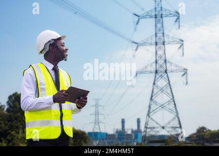 Afrikanischer Ingenieur verwendet ein Tablet, um ein Hochspannungssystem von einem Elektrokraftwerk aus zu betreiben Stockfoto