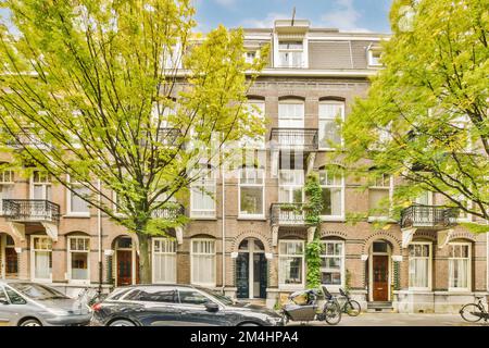 Ein Apartmentkomplex in amsterdam, niederlande, mit Autos, die auf der Straße geparkt sind und grünen Bäumen, die den Vorhof säumen Stockfoto