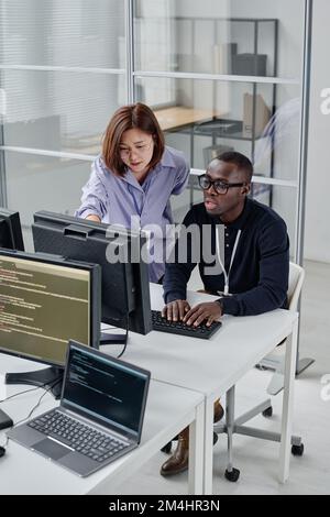 Aus einem großen Blickwinkel können junge Kollegen, die im Team an neuer Software arbeiten, Codes auf dem Computerbildschirm lesen Stockfoto