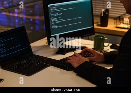 Nahaufnahme eines Programmierers, der ein Computerprogramm mit Codes auf dem Computer entwickelt, während er bis spät in die Nacht im Büro arbeitet Stockfoto