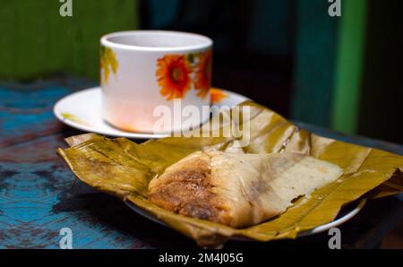 Traditionelle Tamal Pisque gefüllt mit einer Tasse Kaffee auf dem Tisch. Tamal Pisque mit typisch nicaraguanischem Essen. Blick auf eine gefüllte Tamale Stockfoto