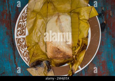 Traditioneller Tamal Pisque gefüllt mit Bananenblatt serviert auf einem Holztisch, typisch zentralamerikanische Küche Tamal Pisque gefüllt. Gefüllte Tamale serviert Stockfoto