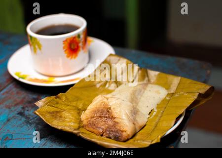 Blick auf eine gefüllte Tamale mit einer Tasse Kaffee auf einem Holztisch, traditionelle Tamal Pisque gefüllt mit einer Tasse Kaffee auf dem Tisch. Stockfoto