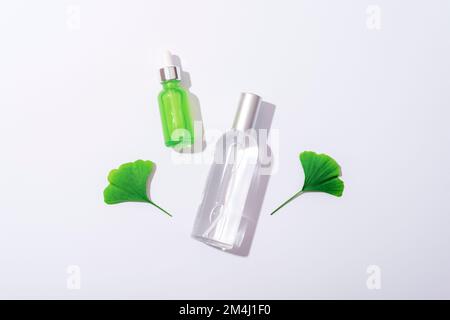 Kosmetikflaschen mit Serum und tonischen und grünen Ginkgo-biloba-Blättern auf weißem Hintergrund, scharfe Schatten. Naturkosmetik-Konzept. Draufsicht, flach liegend Stockfoto