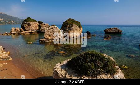 Banana Beach, kleine Felsen vor der Küste im Meer, grüne Vegetation, Meergrün und kristallklar, kleine Felsen sichtbar unter Wasser, wolkenloser blauer Himmel, Zak Stockfoto