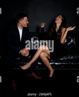 Mann und Frau sitzen auf der Couch, lachende Frau, Abendkleid Stockfoto