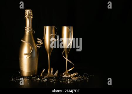 goldene Champagnerflasche und zwei Gläser mit Bändern auf schwarzem Hintergrund und Kopierbereich. Neujahrsfeier und Jubiläumsfeier Stockfoto
