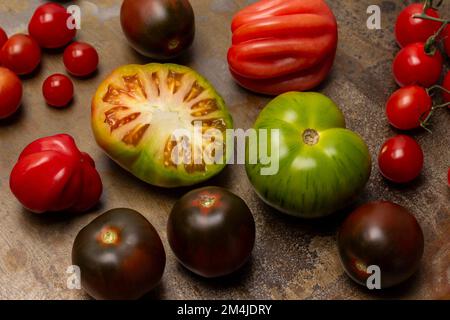 Eine halbe grüne Tomate. Tomaten verschiedener Sorten. Draufsicht. Rostiger Metallhintergrund. Stockfoto