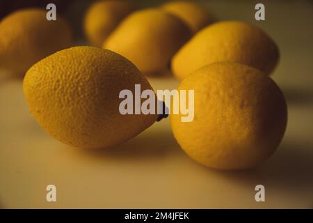 Zitronen auf weißem Tisch mit Obstschale im Hintergrund. Stockfoto