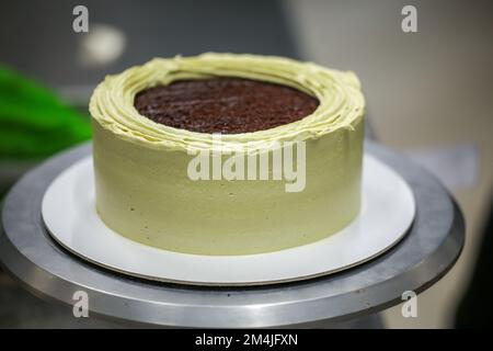 Konditorin mit Spatelkratzer zum Glätten grüner Pistazien-Buttercreme-Milchkuchen - Zubereitung von Hochzeitstorten Stockfoto