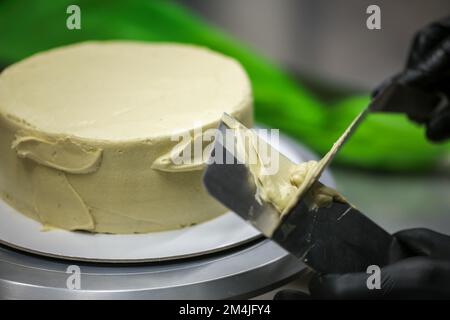 Konditorin mit Spatelkratzer zum Glätten grüner Pistazien-Buttercreme-Milchkuchen - Zubereitung von Hochzeitstorten Stockfoto