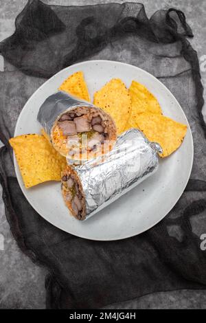 Mexikanischer Rindfleischburrito auf einem kleinen Teller mit Chips Nachos auf dem Teller Stockfoto