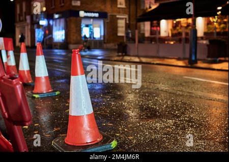 Niedrige Sicht auf Straßenbahnkegel auf nassen Straßen bei Nacht mit unscharfem Hintergrund Stockfoto