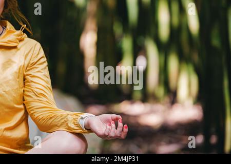 Nahaufnahme der Hand einer Frau, die sich im Lotus im Park entspannt. Unscharfe grüne Bäume im Hintergrund Stockfoto