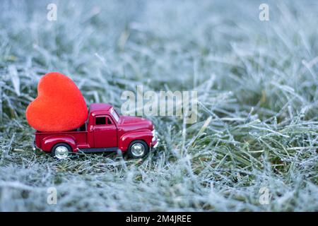 Valentinstag. Roter Auto-Truck und ein Herz drauf. Gras im Frost Stockfoto
