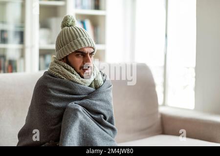 Eiskalter Typ aus dem Nahen Osten, der auf der Couch im Wohnzimmer sitzt Stockfoto