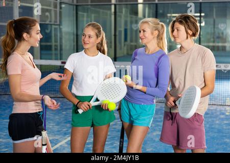 Junge, Mädchen und Erwachsene Frauen im Teenageralter stehen auf dem Padel Court und reden Stockfoto