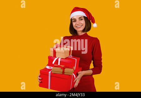 Die Dame mit Weihnachtsmann-Hut hat einen Haufen Neujahrsgeschenke Stockfoto