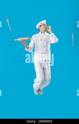 Junger Koch mit Kochutensilien auf blauem Hintergrund Stockfoto