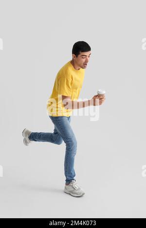 Junger Mann mit einer Tasse Kaffee, der auf hellem Hintergrund springt Stockfoto