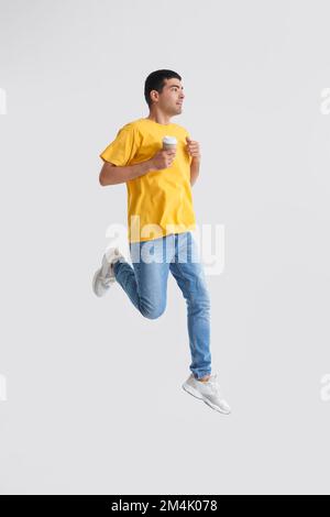 Junger Mann mit einer Tasse Kaffee, der auf hellem Hintergrund springt Stockfoto
