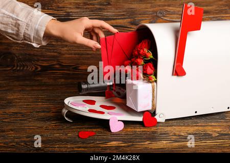 Frau, die Briefe aus dem Briefkasten auf Holzhintergrund nimmt. Valentinstag-Feier Stockfoto