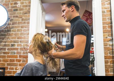 Mittellange Aufnahme eines Friseurs, der die nassen Haare einer Frau hält und an einem Föhn trocknet, Schönheitssalon. Hochwertiges Foto Stockfoto