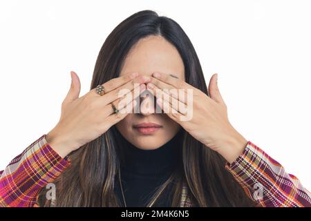 Junge Erwachsene lateinamerikanische Frau mit dunklem, langem Haar vor der Kamera, die ihre Augen mit beiden Händen bedeckt, und kaltem Gesichtsausdruck. Weißer Hintergrund, Kopierbereich, horizontales Studiobild. Hochwertiges Foto Stockfoto