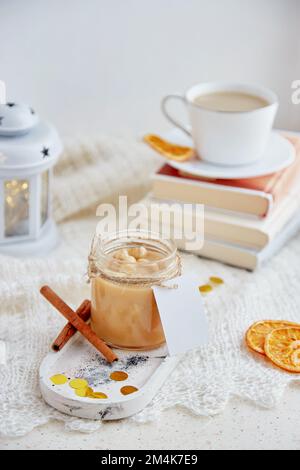 Gemütliches Weihnachtsessen. Ästhetisches, hausgemachtes Haselnusskaramell in Glasgefäß aufgestreut mit Nachahmungsetikett und einer Tasse Kakao. Stockfoto