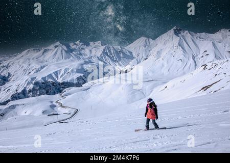 Das Night Snowboarder Girl reitet auf Snowboard unter dem Sternenhimmel in einem großen schneebedeckten Gebirge, Kaukasus, Gudauri Stockfoto