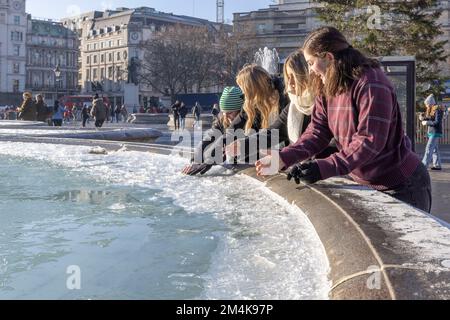 Der Brunnen am Trafalgar Square bleibt bis zum Morgen gefroren. Die Leute haben Spaß mit Eisstücken auf dem Brunnen. Aufnahme am 16. Dezember 2022. ©B Stockfoto