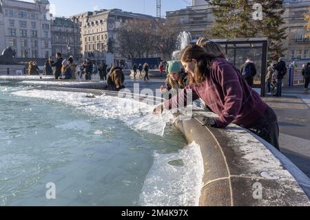 Der Brunnen am Trafalgar Square bleibt bis zum Morgen gefroren. Die Leute haben Spaß mit Eisstücken auf dem Brunnen. Aufnahme am 16. Dezember 2022. ©B Stockfoto