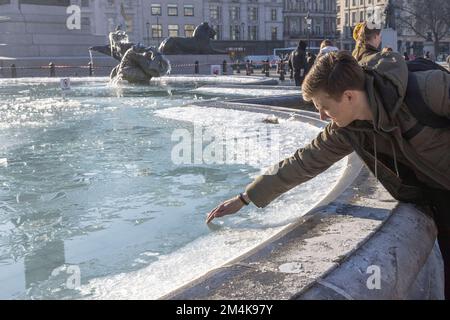 Der Brunnen am Trafalgar Square bleibt bis zum Morgen gefroren. Die Leute haben Spaß mit Eisstücken auf dem Brunnen. Aufnahme am 16. Dezember 2022. ©B Stockfoto