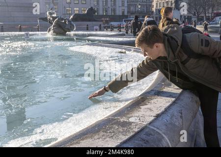 Der Brunnen am Trafalgar Square bleibt bis zum Morgen gefroren. Die Leute haben Spaß mit Eisstücken auf dem Brunnen. Aufnahme am 16. Dezember 2022. ©B Stockfoto