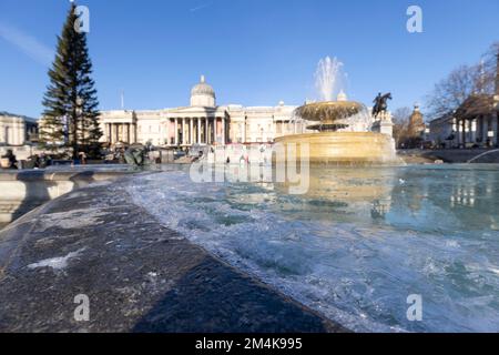 Der Brunnen am Trafalgar Square bleibt bis zum Morgen gefroren. Die Leute haben Spaß mit Eisstücken auf dem Brunnen. Aufnahme am 16. Dezember 2022. ©B Stockfoto