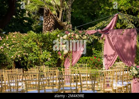 Der Hochzeitsbogen ist mit pinkfarbenen und weißen Blumen dekoriert. Ort für die Hochzeitszeremonie in Farbe. Hochzeitszeremonie im Freien. Stockfoto