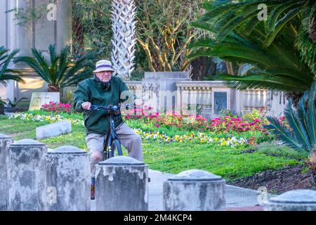 NEW ORLEANS, LA, USA - 16. DEZEMBER 2022: Senior Citizen fährt willkürlich auf dem Gehweg vor dem Audubon Park mit dem Fahrrad statt auf dem Radweg Stockfoto