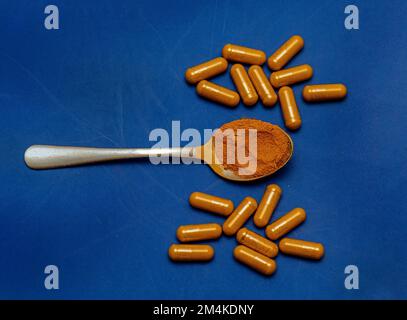 Kurkuma-Nahrungsergänzungspillen mit Curcumin-Gewürzpulver in Metalllöffel isoliert auf blauem Hintergrund Stockfoto