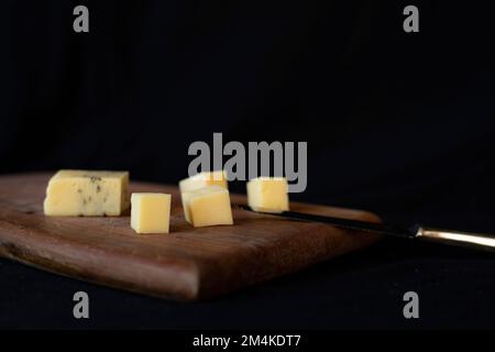 Eine Nahaufnahme von Würfeln verschiedener Käsesorten und einem Messer auf einem Schneidebrett Stockfoto