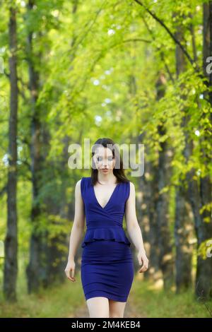 Eine Frau in blauem Kleid, die im Herbst auf einer Lindenallee spaziert. Pfad unter gelben Bäumen mit herbstlichen Blättern. Sonniger Herbsttag. Die Sonnenstrahlen Stockfoto